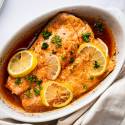 Salmon recipe for lemon pepper salmon served in a white baking dish with sliced lemons and parsley.