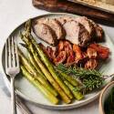 A close-up view of a dinner plate featuring juicy rosemary-seasoned steak slices, perfectly roasted asparagus, and golden sweet potato wedges, plated elegantly with a sprig of fresh rosemary and accompanied by a fork and knife