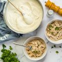 Skinny Alfredo sauce in a large pan with a wooden spoon and served in two bowls with spaghetti and parsley.