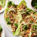 A platter of lettuce wraps filled with shredded chicken, carrot and cucumber julienne, topped with sesame seeds and fresh cilantro.