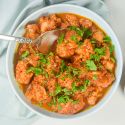 Slow cooker chicken and cauliflower tikka masala in a bowl with cilantro and spices on he side.