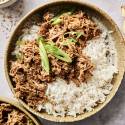 Shredded sesame beef over rice with green onion garnish.