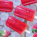 Bright red strawberry popsicles on ice, accompanied by fresh strawberries, create a refreshing summer treat scene.