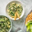 Bowls of creamy spinach, artichoke, and kale dip served with crispy breadsticks and fresh celery sticks for dipping.