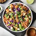 A vibrant salad with purple cabbage, carrots, edamame, chicken, and cilantro, drizzled with peanut sauce and topped with cashews.