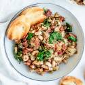 Tuscan white bean skillet with spinach, tomatoes, artichokes, onions, and garlic in a bowl with toast.
