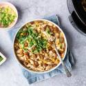 A hearty bowl of chicken chili topped with fresh cilantro and sliced green onions. A dish of green onions and fresh cilantro beside it, exuding a cozy feel.