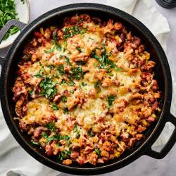 Taco casserole with pinto beans, onions, peppers, turkey, corn, salsa, and melted cheese with chips, cilantro, and jalapeno on the side.