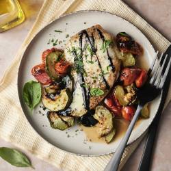 A plate of caprese chicken with roasted zucchini and tomatoes, topped with balsamic glaze and fresh basil.