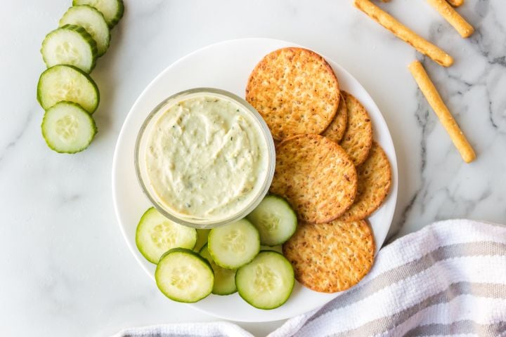 Avocado ranch dip with Greek yogurt served in a small bowl with sliced cucumbers and crackers.