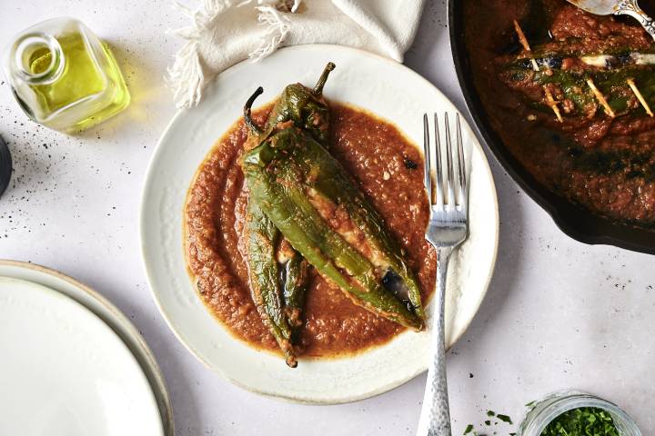 Chiles rellenos served on a plate with a rich tomato-based sauce, garnished with cilantro and a drizzle of oil.