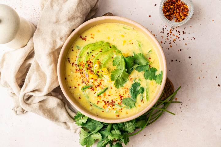 Creamy corn soup garnished with avocado slices, cilantro, and red pepper flakes.