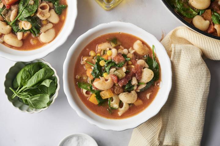 A cozy bowl of garden minestrone packed with shell pasta, corn, spinach, white beans, and vibrant vegetables in a savory tomato broth.