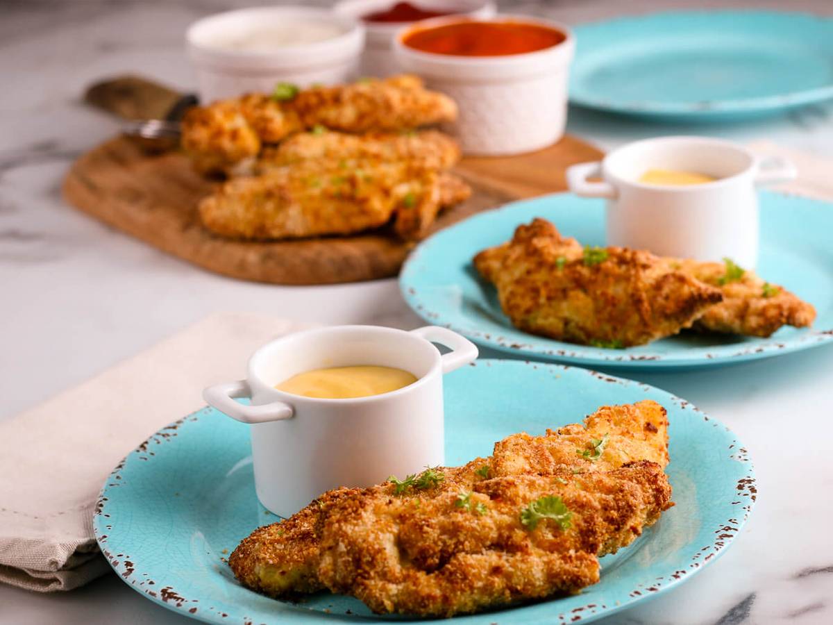 Air fryer chicken tenders with honey mustard sauce on two blue plates.