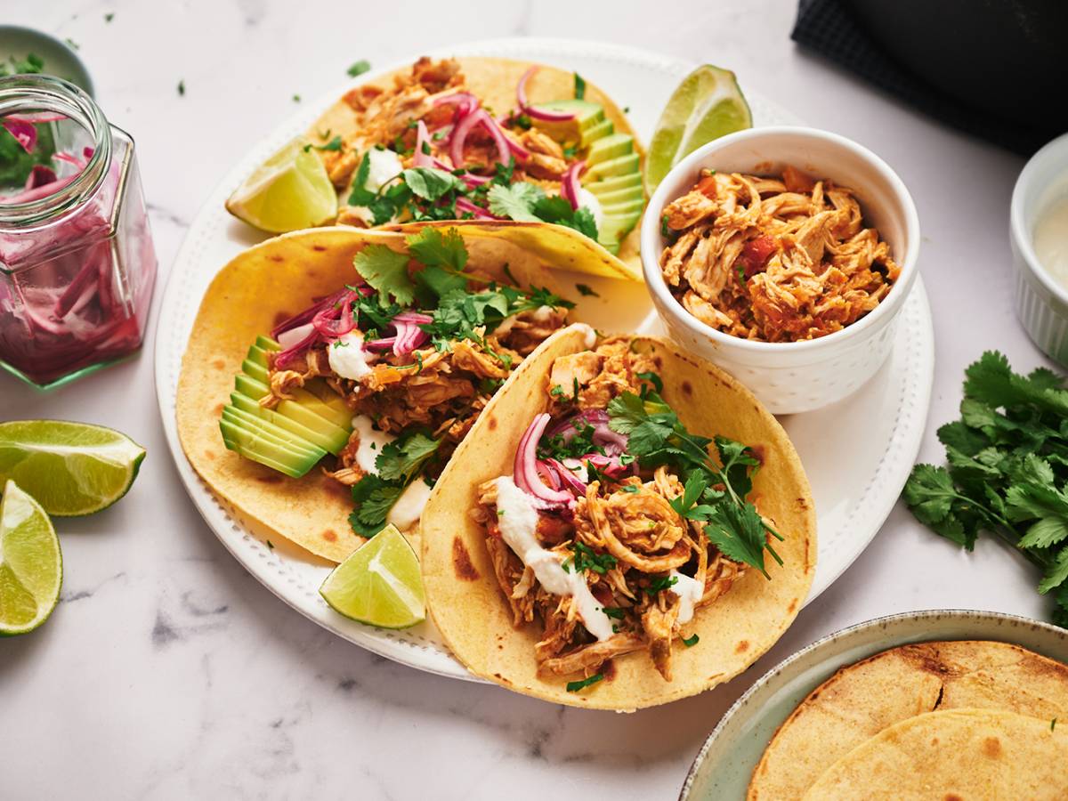 3 Shredded chicken tacos with avocado, pickled onions, cilantro, and limes served on a round plate.